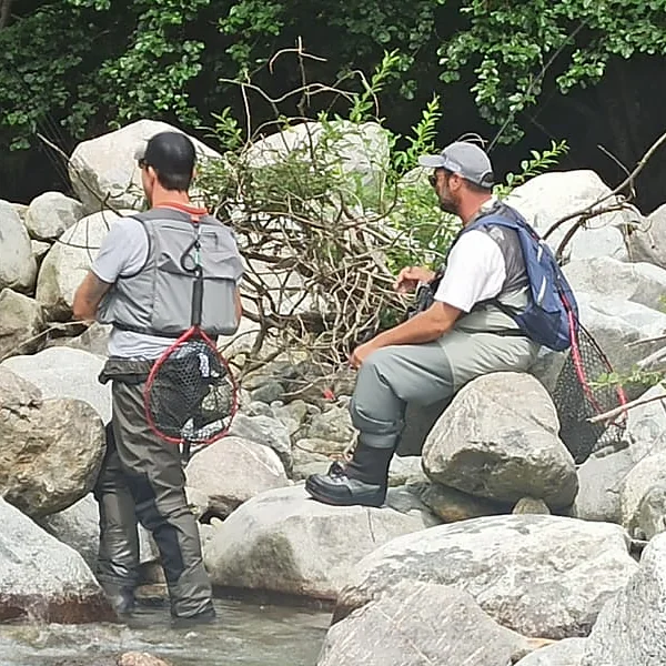 Due pescatori su un torrente della Valle Camonica durante una sessione tecnica: uno lavora in acqua, l'altro prepara il finale